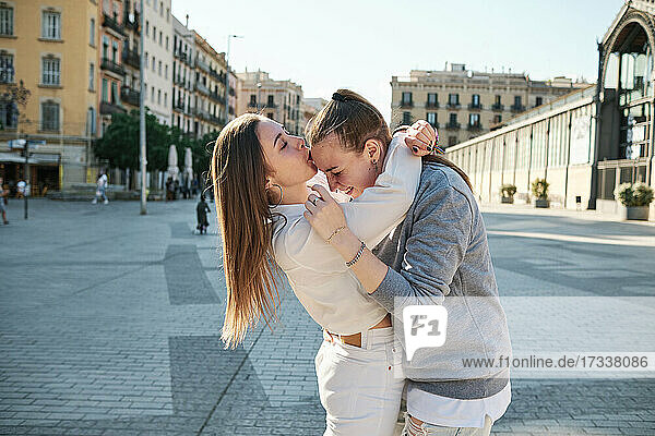 Frau mit Arm um küssende Freundin auf die Stirn in der Stadt stehend