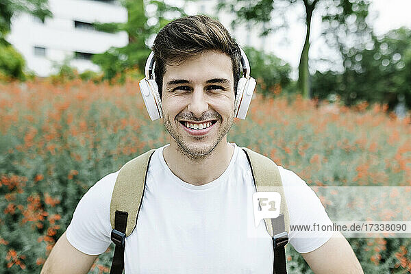 Smiling young man listening music through headphones amidst meadow