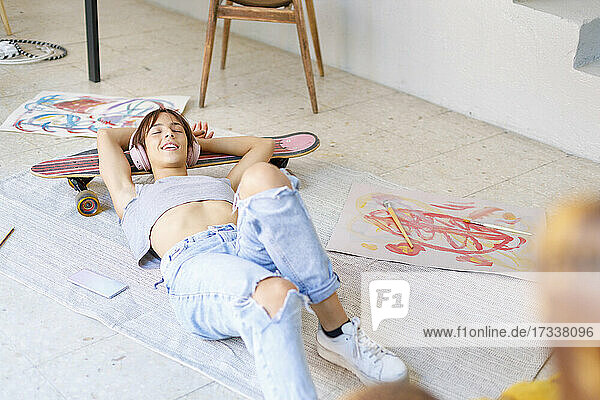 Young female painter with eyes closed relaxing on skateboard in studio