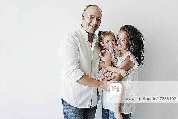 Smiling man standing by woman carrying daughter in front of white background
