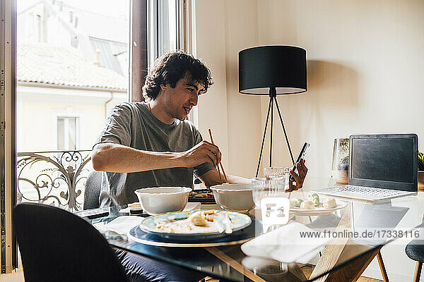 Man using mobile phone while having lunch at home