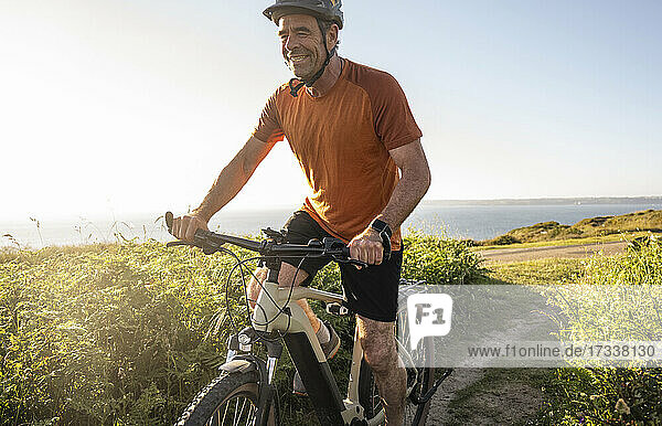 Happy sportsman cycling amidst green plants at sunset