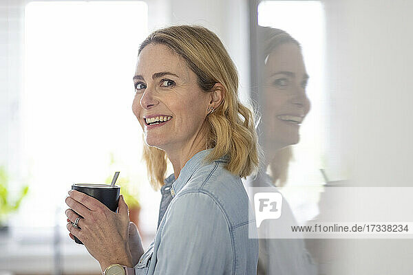 Smiling blond woman holding mug at home