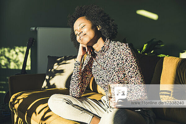 Junge Frau mit Trinkglas träumt beim Sitzen zu Hause