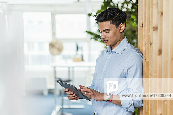 Männlicher Fachmann  der ein digitales Tablet benutzt  während er sich an die Wand lehnt