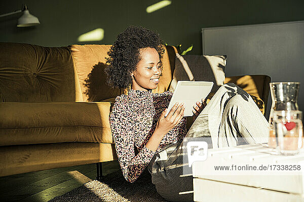 Lächelnde Frau  die ein digitales Tablet benutzt  während sie zu Hause im Wohnzimmer sitzt