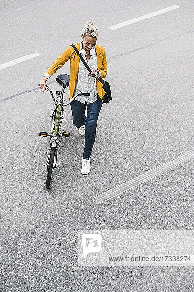Berufstätige Frau  die ein Mobiltelefon benutzt  während sie mit dem Fahrrad auf der Straße geht