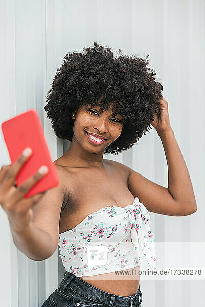 Lächelnde junge Frau  die ein Selfie mit ihrem Mobiltelefon vor einer Wand macht
