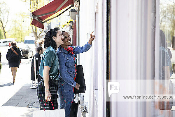 Smiling lesbian couple window shopping while standing on footpath