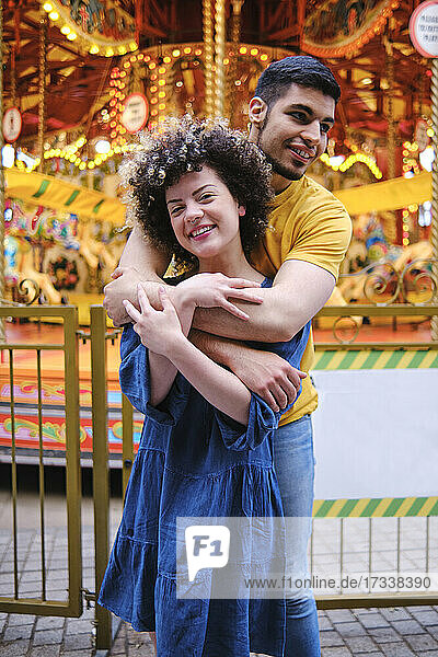 Happy young couple standing with arms around at amusement park