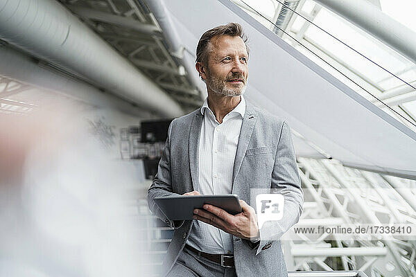 Nachdenklicher männlicher Fachmann  der ein digitales Tablet hält  während er im Büro steht
