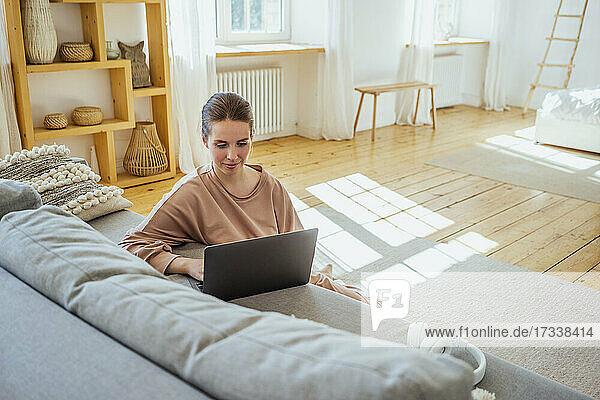 Junge Geschäftsfrau  die einen Laptop benutzt  während sie zu Hause auf dem Boden sitzt