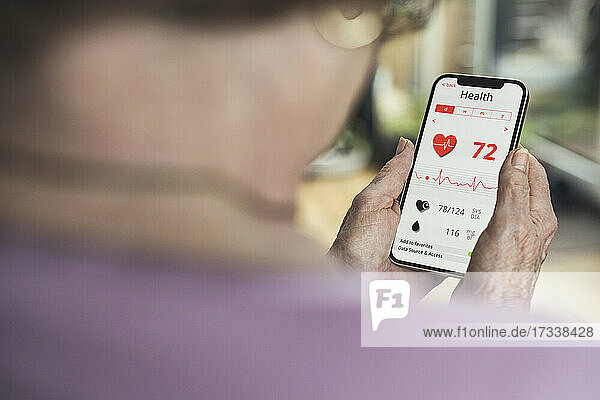 Senior woman checking pulse trace on mobile phone at home