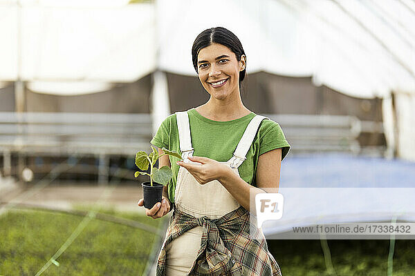 Smiling female farm worker standing with potted plant