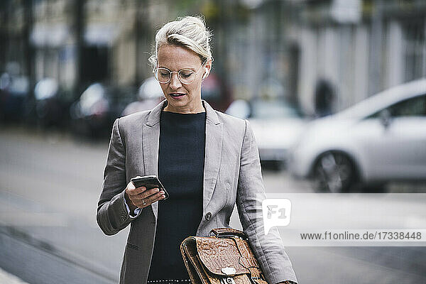 Blond female commuter holding bag while using smart phone