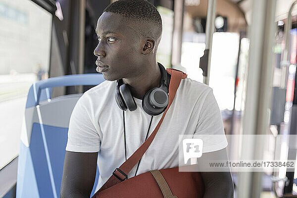 Young man with headphones looking through window in bus