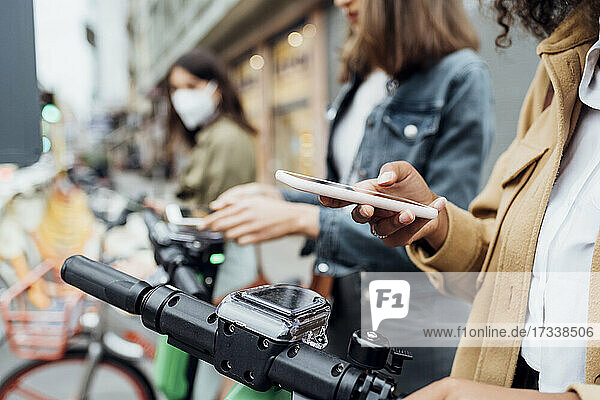 Woman unlocking bicycle through smart phone with friends standing in background