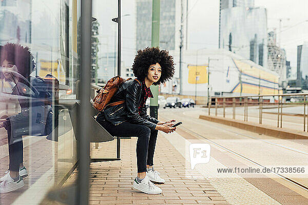 Frau mit Mobiltelefon an der Straßenbahnhaltestelle