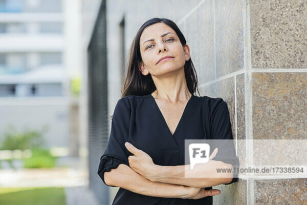 Geschäftsfrau mit verschränkten Armen  die sich an die Wand lehnt  während sie vor einem Bürogebäude steht