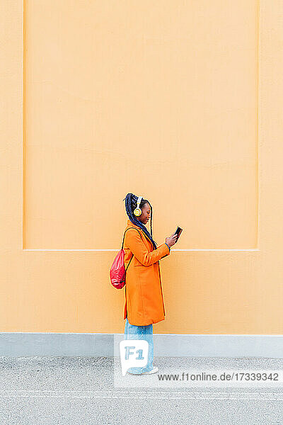 Italien  Mailand  Frau mit Kopfhörern und Smartphone vor orangefarbener Wand