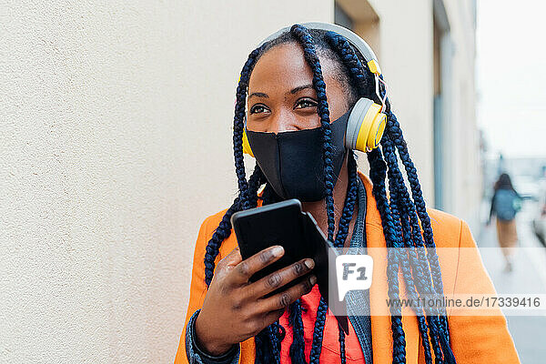 Italien  Mailand  Modische Frau mit Gesichtsmaske  Kopfhörer und Smartphone