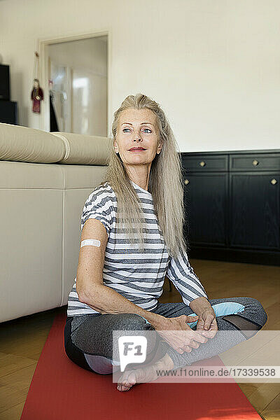 Austria  Vienna  Senior woman with adhesive bandage on arm sitting on yoga mat