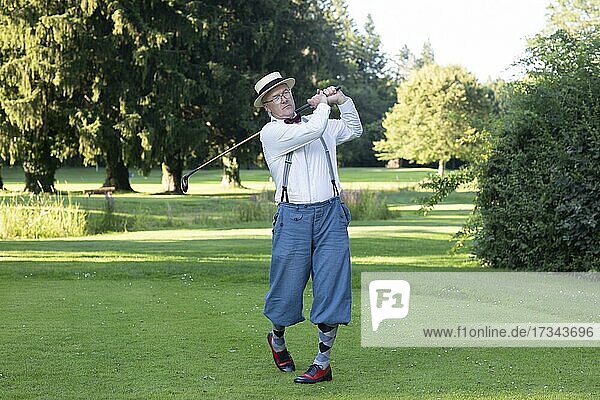 Older man in straw hat and knickerbockers playing hickory golf on a golf course