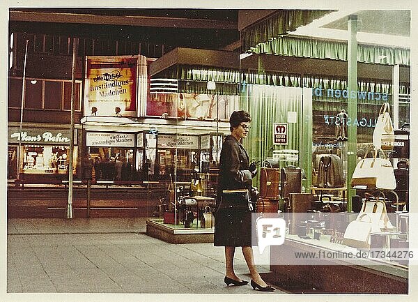 Stuttgart at night in 1963: A young woman with a coat and handbag looks at the display of handbags and suitcases in a leather goods shop  in the back a cinema with the announcement of the film Ein fast anständiges Mädchen starring Liselotte Pulver  Baden-Württemberg  Germany  Europe
