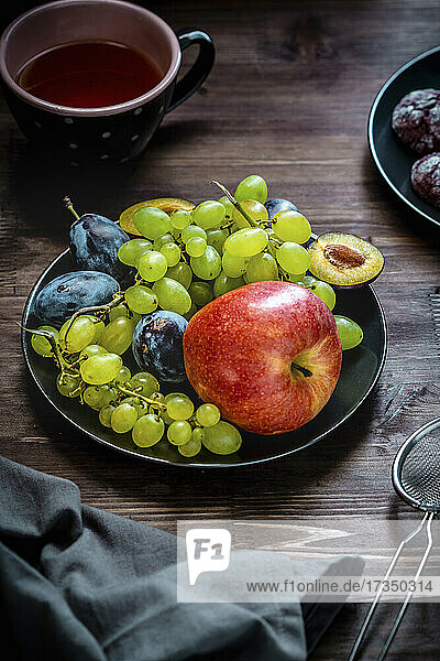 Teller mit Früchten - Apfel  weiße Trauben und Pflaumen