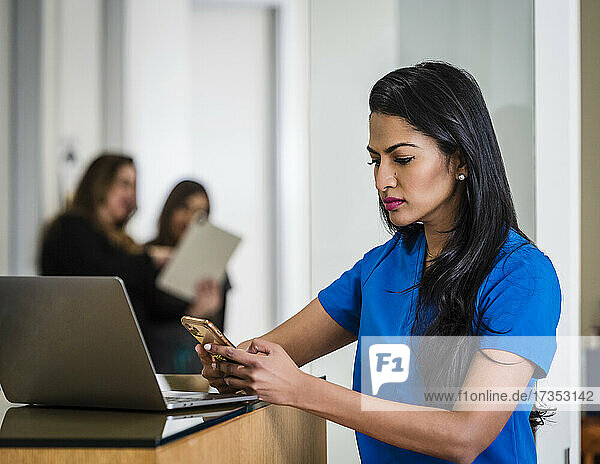 Female doctor with smart phone and laptop at reception desk