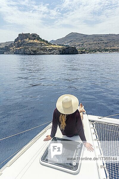 Junge Frau mit Sonnenhut sitzt auf einem Boot  Lindos  Rhodos  Dodekanes  Griechenland  Europa