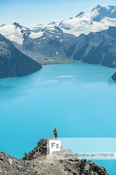 Junger Mann steht auf einem Felsen  blickt in die Ferne  Blick auf Berge und Gletscher mit türkisblauem See Garibaldi Lake  Gipfel Panorama Ridge  Guard Mountain und Deception Peak  Garibaldi Provincial Park  British Columbia  Kanada  Nordamerika