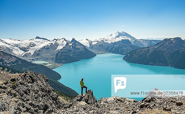 Young man standing on a rock  looking into the distance  view of mountains and glacier with turquoise blue lake Garibaldi Lake  peaks Panorama Ridge  Guard Mountain and Deception Peak  Garibaldi Provincial Park  British Columbia  Canada  North America