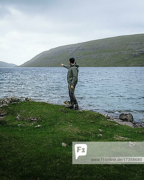 Hiker standing on the shore of Lake Leitisvatn pointing into the distance  Vagar  Faroe Islands  Europe