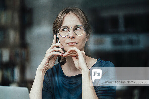 Weibliche Freiberuflerin mit Hand am Kinn  die in einem Café mit ihrem Mobiltelefon spricht