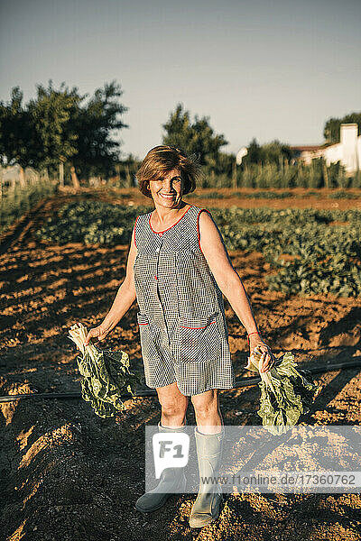 Lächelnde Landarbeiterin hält Gemüse auf einem Feld