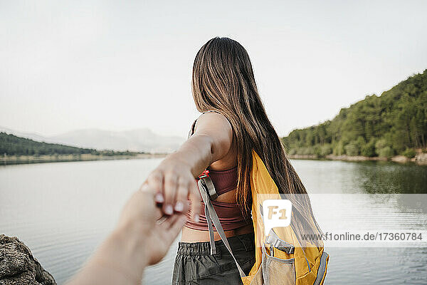 Weibliche Rucksacktouristin hält die Hand ihres Freundes am Seeufer