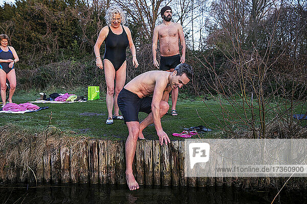 Mann taucht Füße in Fluss mit Freunden im Hintergrund