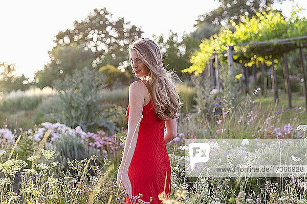 Junge schöne Frau in rotem Kleid geht inmitten von Blumen
