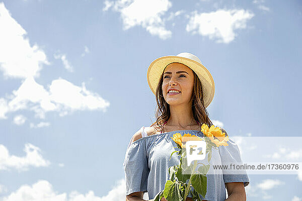 Junge Frau mit Hut und Sonnenblumen in der Hand an einem sonnigen Tag