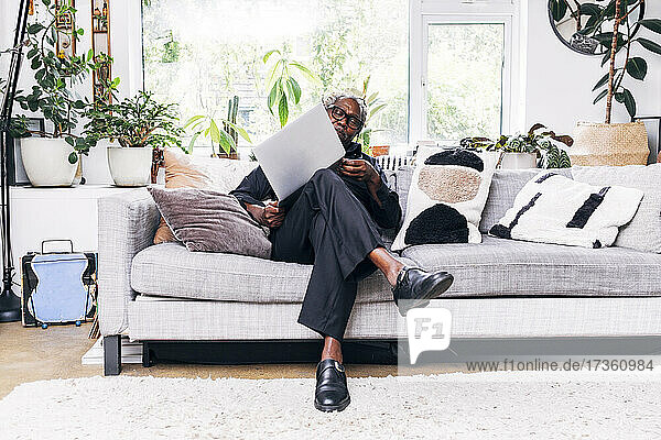 Senior businessman examining laptop while sitting on sofa at home