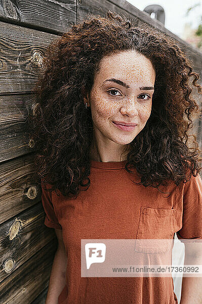 Schöne junge Frau mit lockigem Haar an einer Holzwand