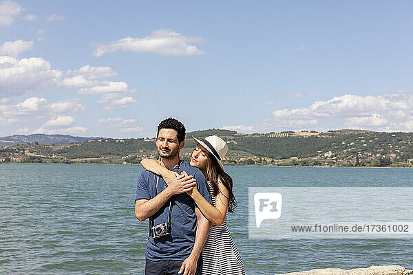 Woman embracing boyfriend from behind in front of Lake Trasimeno