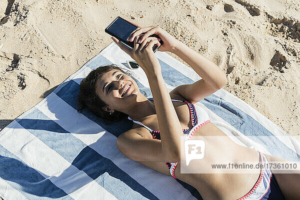 Lächelnde junge Frau  die ein Mobiltelefon benutzt  während sie sich am Strand entspannt