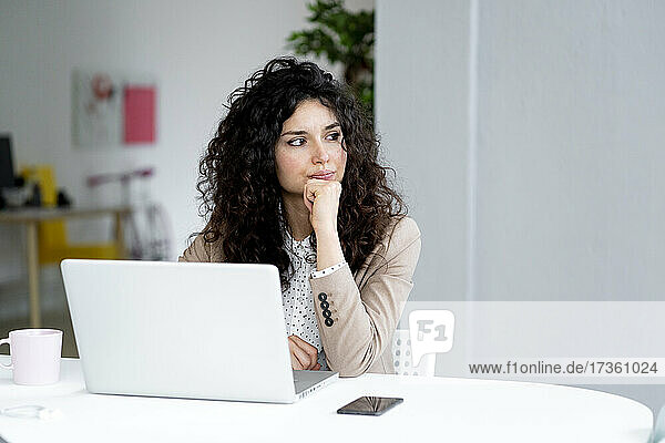 Businesswoman looking away while sitting with hand on chin at desk in office