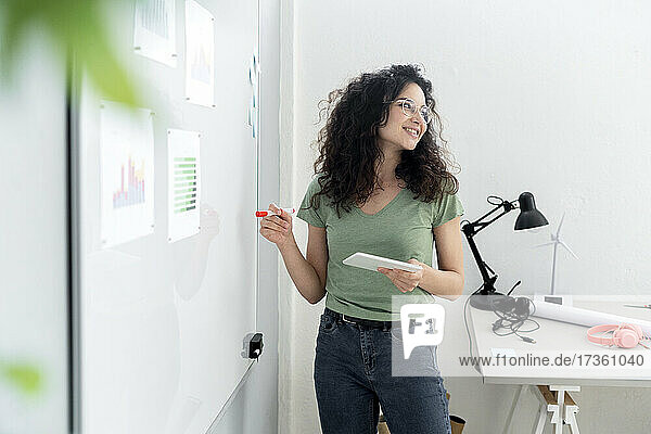 Geschäftsfrau mit digitalem Tablet  die eine Geschäftsstrategie auf einem Whiteboard im Büro plant