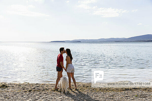 Couple kissing each other while standing by pet at lakeshore