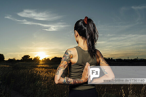 Frau mit hinter dem Rücken verschränkten Händen übt Yoga auf dem Lande