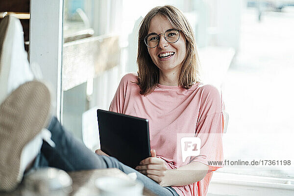 Fröhliche Freiberuflerin sitzt mit digitalem Tablet in einem Cafe