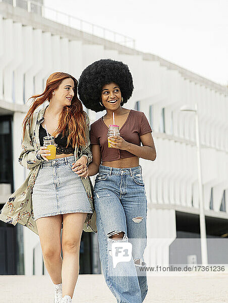 Happy young female friends holding hands while walking in city